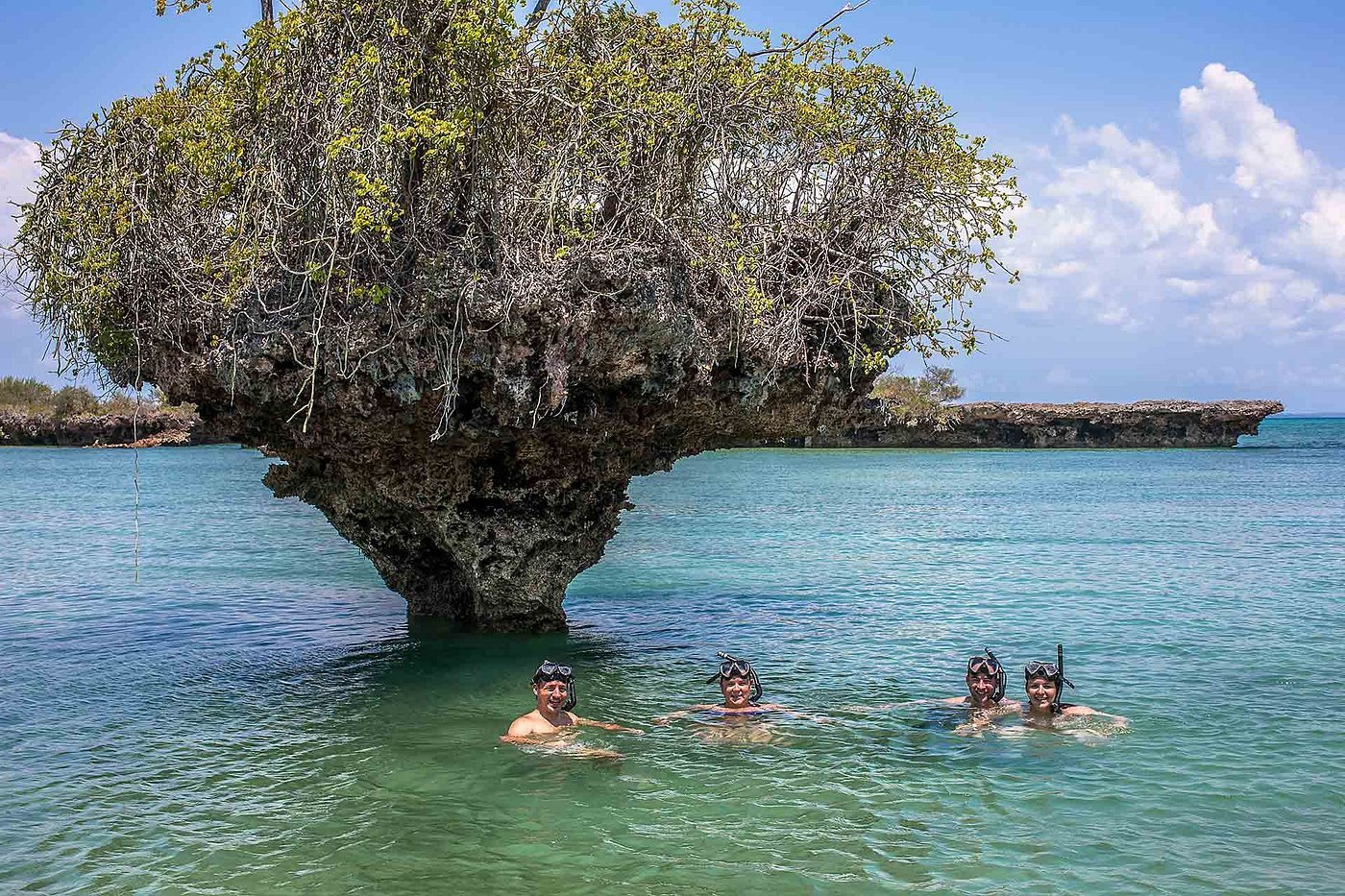 Swimmers beside a coral rock formation in clear Zanzibar water